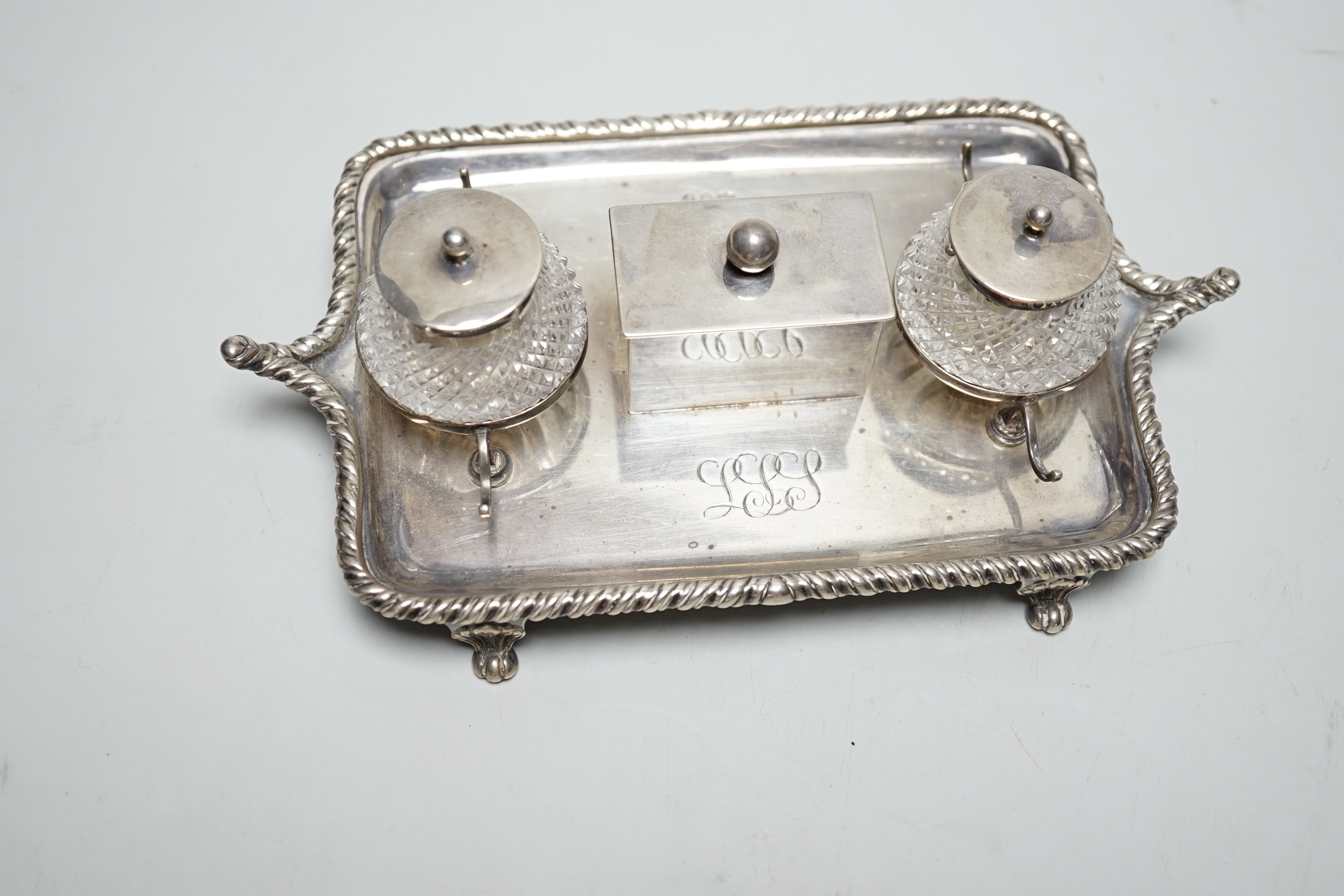 A late Victorian silver rectangular inkstand, with two mounted cut glass wells, central lidded compartment and two pen rests, Edward Hutton, London, 1890, 19cm, weighable silver 9oz.